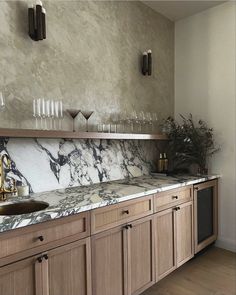 a marble counter top in a kitchen with wooden cabinets and wine glasses on the shelves