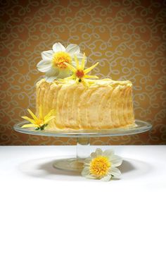 a cake with yellow icing and daisies on top sitting on a glass plate