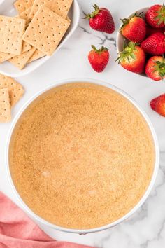 a bowl of dip surrounded by strawberries and crackers