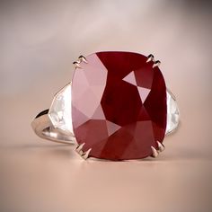 a large red and white stone ring on top of a beige surface with two diamonds