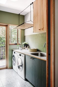 a washer and dryer in a kitchen with green tiles on the walls, wooden cabinets