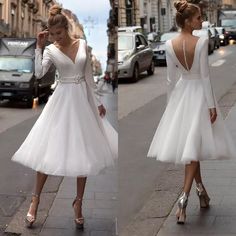 a woman wearing a white dress and heels on the sidewalk in front of some cars