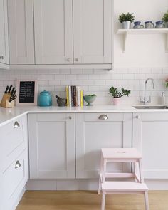 a kitchen with white cabinets and pink stool in front of the counter top, next to a sink