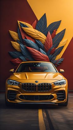 a yellow sports car parked in front of a wall with colorful leaves on it's side