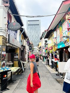 a woman in a red hat is walking down the street with shops on both sides