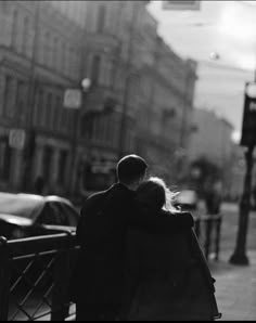 a man and woman standing next to each other on a sidewalk in front of traffic lights