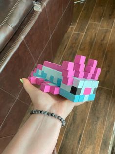 a hand holding a small pink and blue blocky paper toy in it's palm