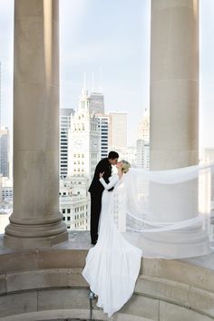 the bride and groom are posing for their wedding photo in front of some tall buildings