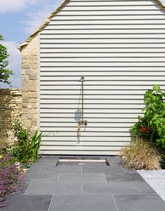 an outdoor shower in front of a white building with plants and flowers on the side