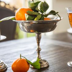 an orange sitting in a silver bowl on top of a table next to two wine glasses