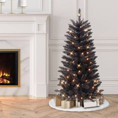 a black christmas tree with lights and presents in front of a fireplace