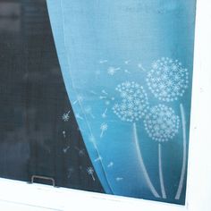 a dandelion drawn on the side of a window sill with blue curtains