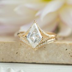 a white diamond ring sitting on top of a piece of stone next to a flower