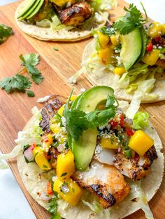 three tacos with chicken, avocado, and mango salsa on them sitting on a cutting board