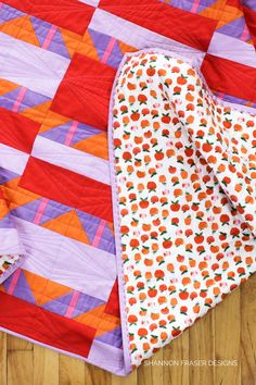 an orange and purple quilt on top of a wooden floor next to a piece of cloth