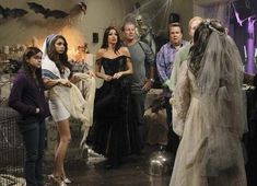 a group of people dressed up as witches and brides in a living room with halloween decorations on the walls