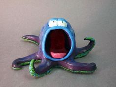 an octopus figurine with its mouth open and tongue out on a gray surface