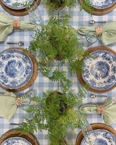 the table is set with blue and white plates, silverware, green plants and napkins