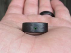 a man's hand holding a black ring with a green stone in it and the middle