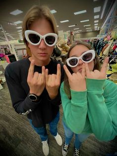 two girls wearing sunglasses making the peace sign with their hands in front of her face