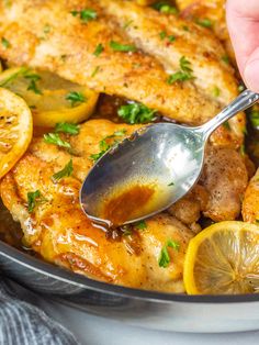 someone is spooning some chicken with lemons and parsley on the side in a skillet