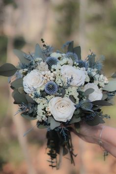 a bridal bouquet in someone's hand with white flowers and greenery on it