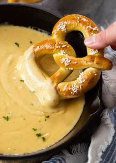 a pretzel being dipped with cheese sauce in a skillet