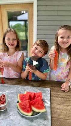 three young children are eating watermelon on the table