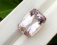 a fancy pink diamond sitting on top of a white piece of cloth with green leaves in the background