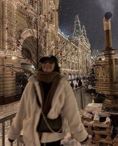 a woman is standing in front of a building with christmas lights on it and snow falling all around her