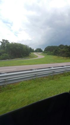 the view from inside a vehicle looking at an empty road and grassy area with trees