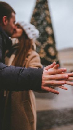 a man and woman standing next to each other near a christmas tree with their hands out