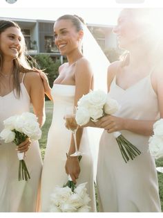 three bridesmaids in white dresses holding bouquets and smiling at each other with the sun shining on them