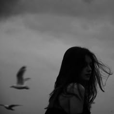 a woman with long hair standing in front of a seagull flying over her head