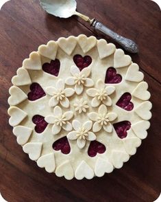 a pie crust with hearts and flowers on it sitting on a wooden table next to a spoon