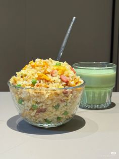 a glass bowl filled with rice and vegetables next to a green cup on a table