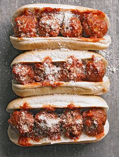 three hot dogs covered in sauce and meatballs on buns with sprinkled parmesan cheese