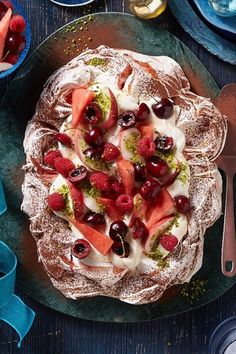 a cake with fruit and cream toppings sitting on top of a blue plate next to silverware