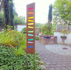 a wooden sign sitting on the side of a brick walk way next to a garden