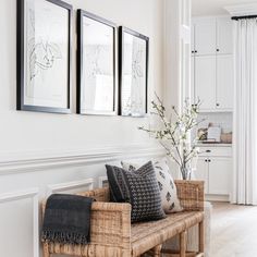 a bench with some pillows on it in front of two framed pictures and a potted plant