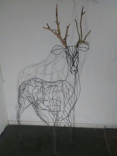 a wire sculpture of a deer standing next to a wall