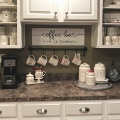 a kitchen counter with coffee mugs hanging on the wall and an open shelf above it