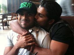 two men are hugging each other in a restaurant together, one is wearing a hat and the other has his arms around him