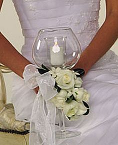 a woman in a white dress holding a wine glass with flowers and a candle on it