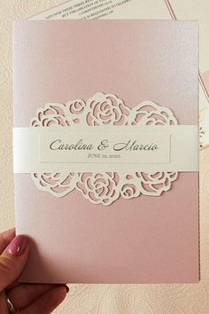 a hand holding a pink wedding card with white lace on the front and bottom,