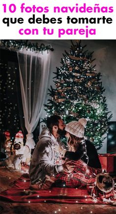 two people sitting on the ground in front of a christmas tree