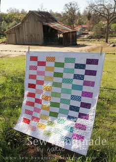 a quilt is hanging on a fence in front of an old barn with a colorful checkerboard pattern