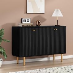 a black cabinet with two gold handles and some books on the top, in front of a pink wall