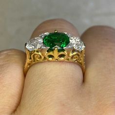 This three-stone ring features a 1.65 carat natural emerald, round cut and set in prongs. On either side of the center stone are old European cut diamonds with a combined weight of 1.08 carats, K-L color and VS1 clarity. Smaller old European cut diamonds are set on the prongs on either side of the emerald and along the shoulders. The under-gallery is decorated with an openwork design. This ring is handcrafted in platinum on 18k yellow gold.
The approximate measurements of the emerald are 7.50mm Luxury Oval Emerald Ring With Three Stones, Luxury Oval Three Stone Emerald Ring, Luxury Green Three Stone Diamond Ring, Luxury Green Diamond Three Stone Ring, Luxury Green Three-stone Diamond Ring, Luxury Three-stone Green Diamond Ring, Heirloom Oval Emerald Ring With Three Stones, Heirloom Three Stone Emerald Ring, Heirloom Three Stone Emerald Diamond Ring