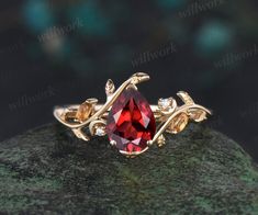 a gold ring with a red stone surrounded by leaves and diamonds on a green rock